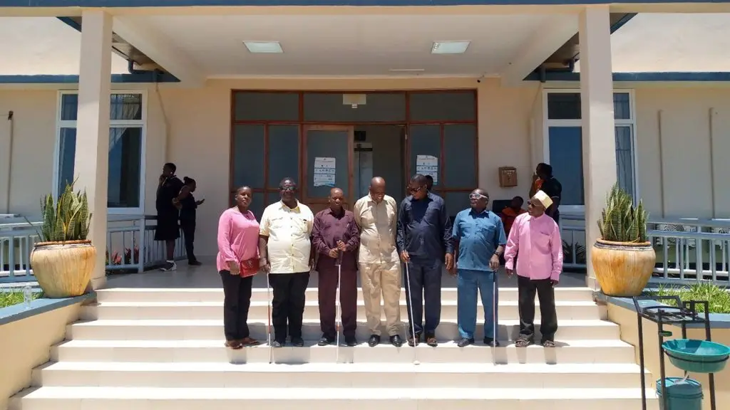 Seven TLB leaders stand on the steps of an office building, most holding white canes.